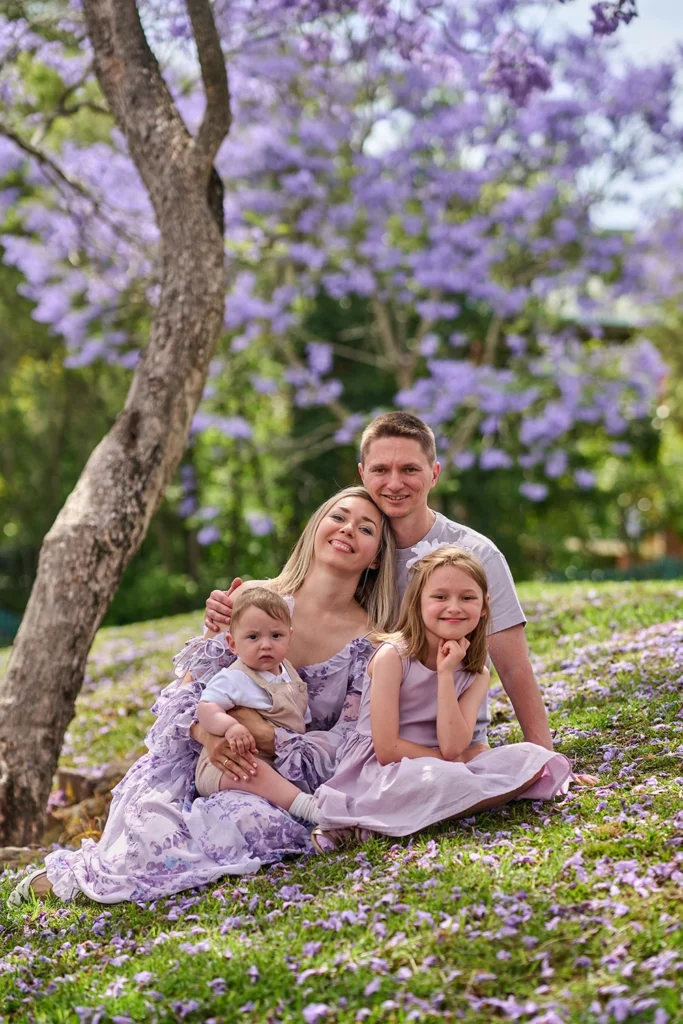 Young family with two children sitting under blooming purple jacaranda trees