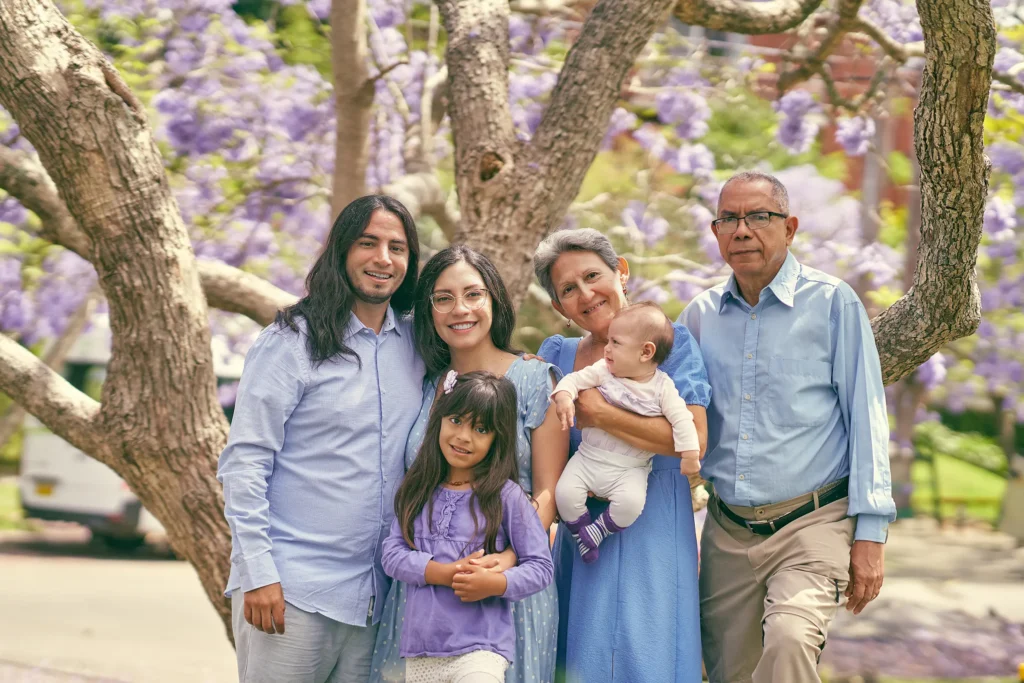 Extended family with grandparents, parents, and baby under blooming jacaranda trees