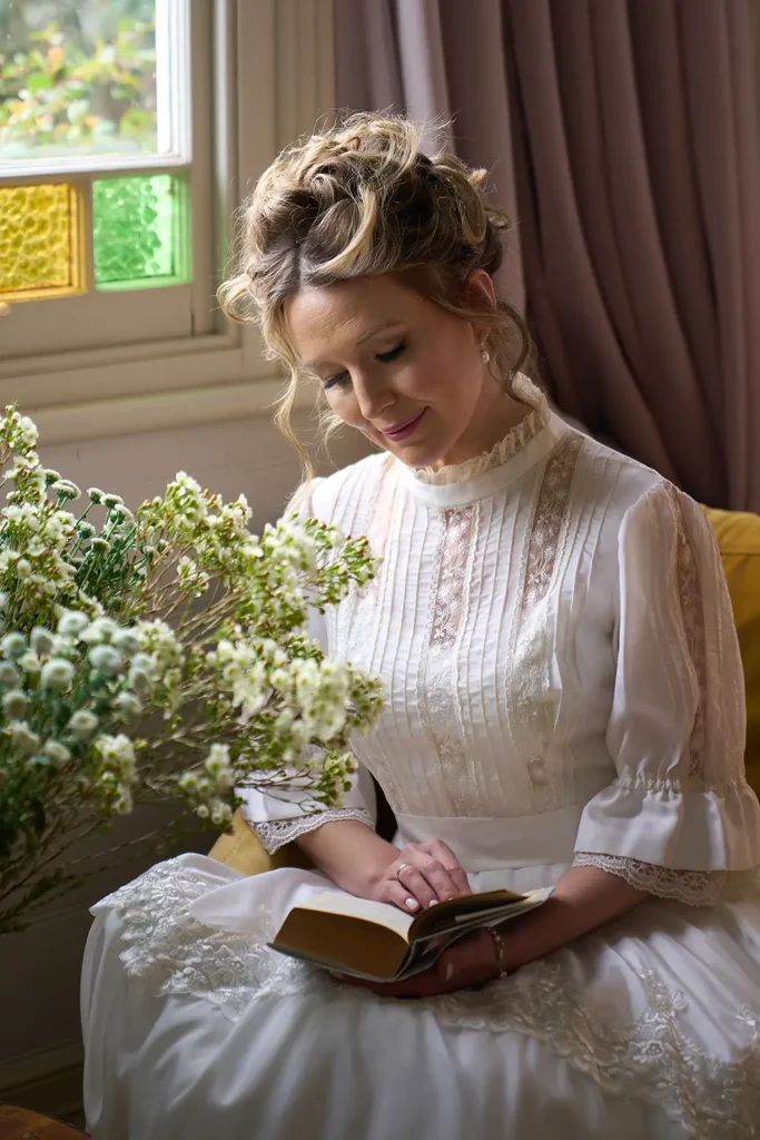 Woman in full Bridgerton style look reading book in armchair with flowers, Sydney photoshoot