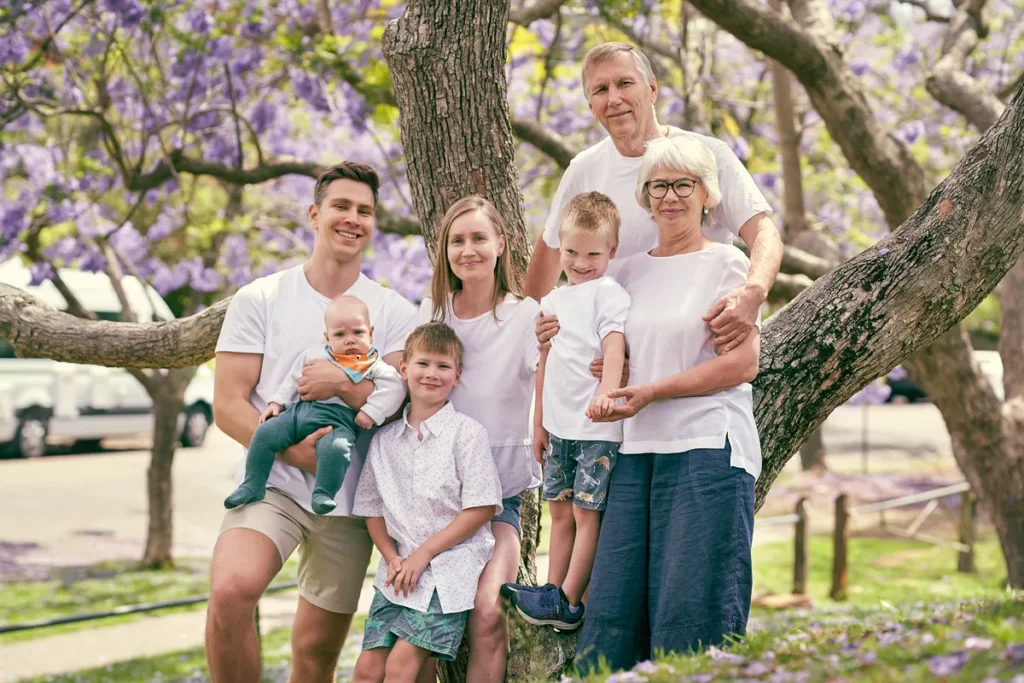 Extended family with three children posing under blooming purple jacaranda trees.