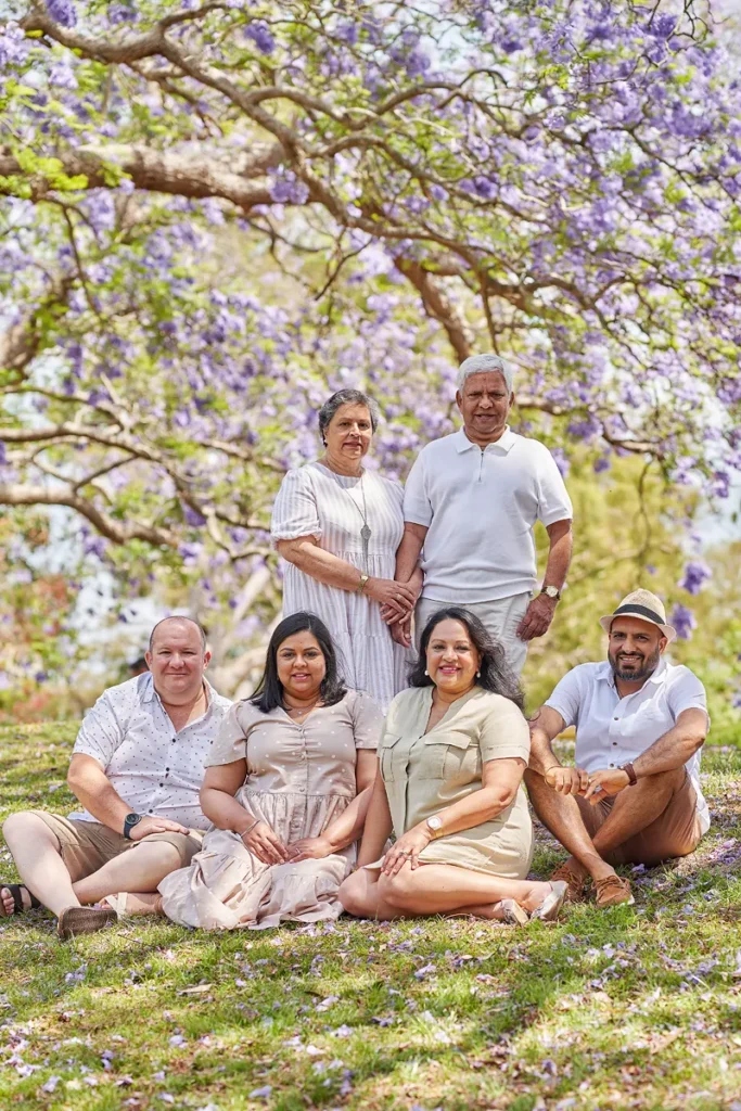 Extended family group sitting on ground together in Parramatta park during Jacaranda