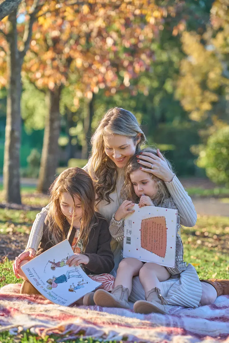 mum and two daughters sitting on blanket reading a book