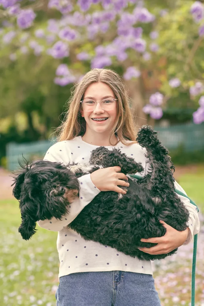 Teenage girl hugging dog in booming jacaranda park