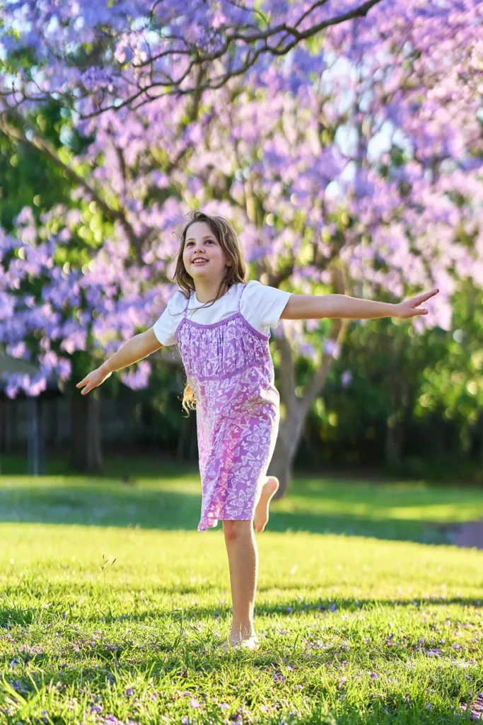 Girl skipping across grass under purple blossoms