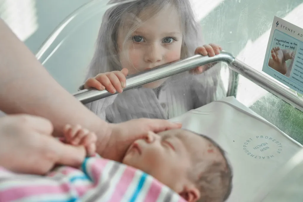 Toddler looking curiously into hospital bassinet