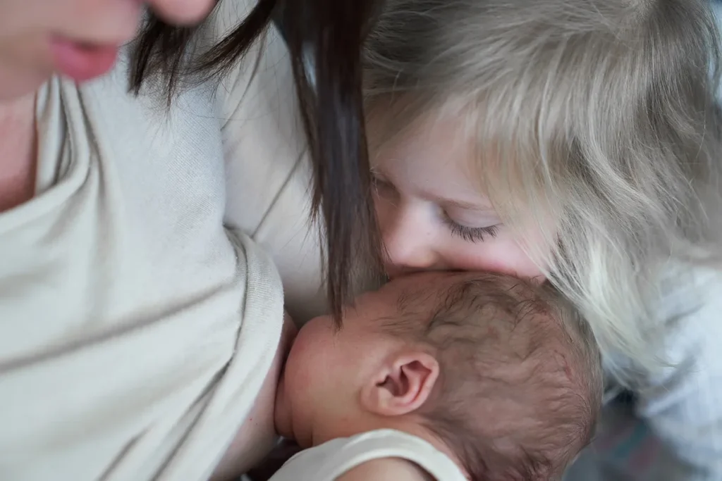 Mother and toddler kissing newborn baby
