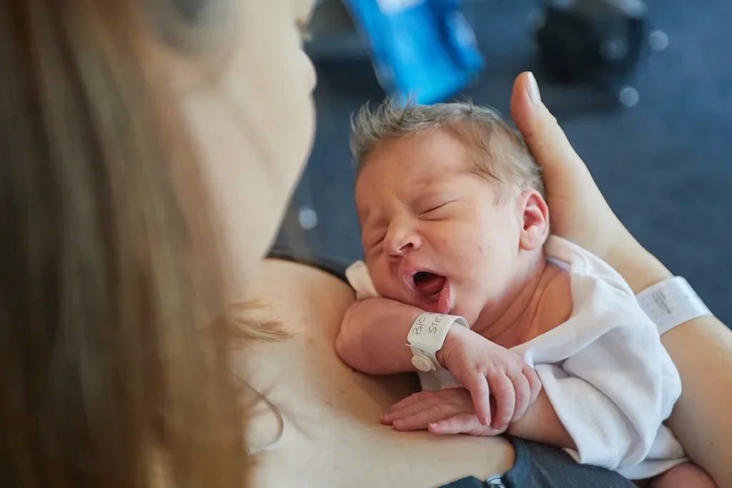 Newborn yawning while held in mother's arms