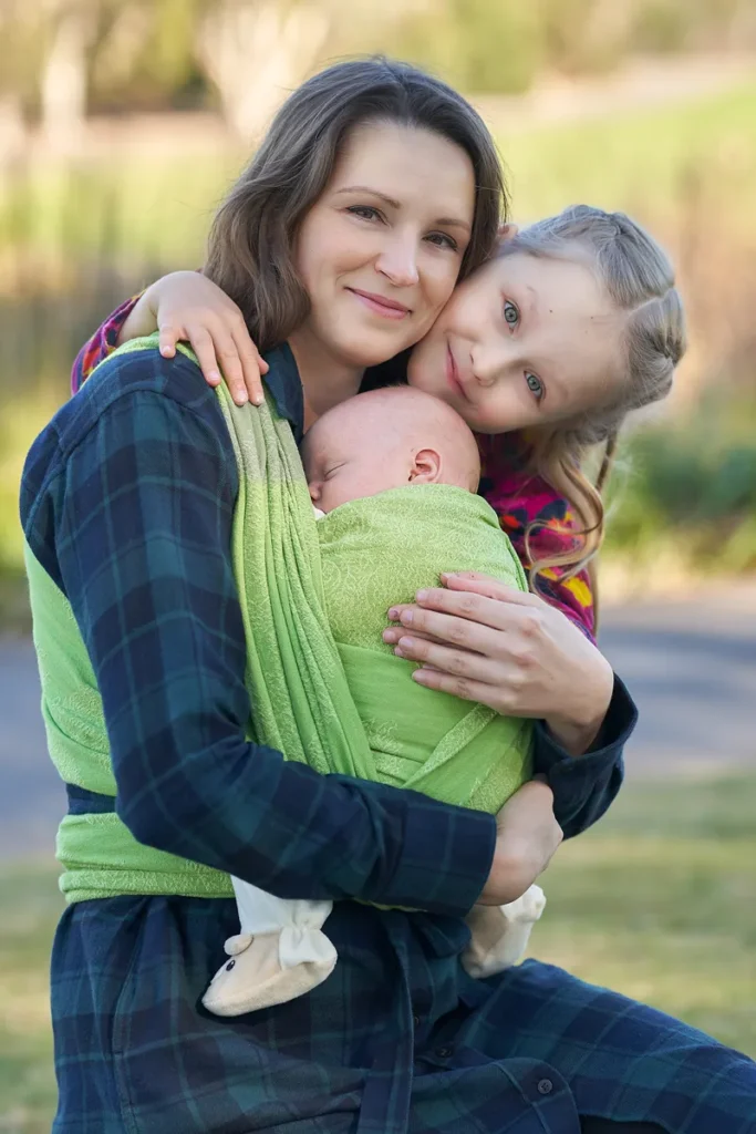 Mother holding baby son in a wrap carrier with daughter hugging her at Mount Annan.