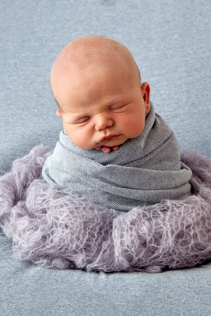 baby wrapped in lavender sleeping on grey backdrop