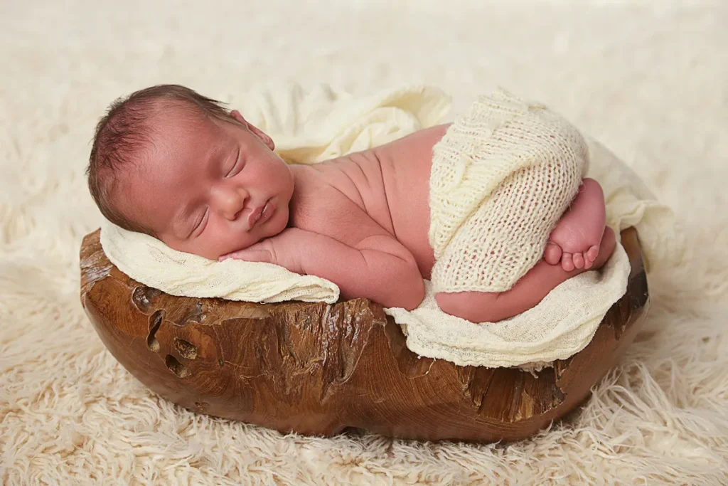 newborn sleeping on stomach inside rustic wooden bowl