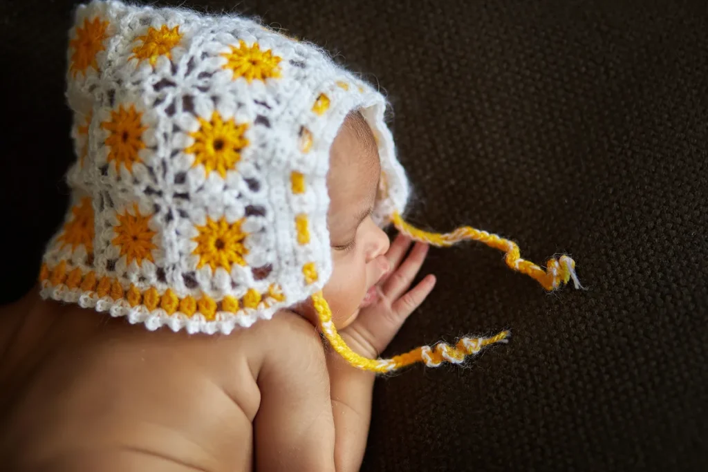 newborn in floral crochet bonnet on dark backdrop