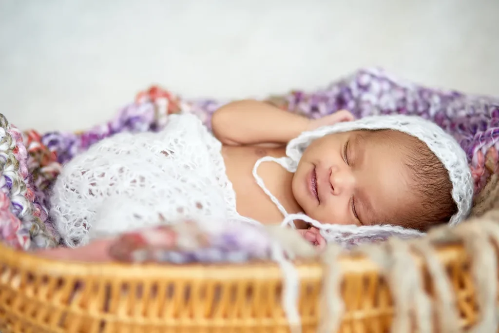newborn in white bonnet curled in wicker basket