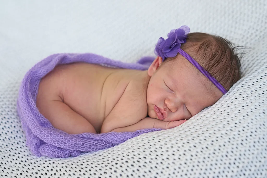 newborn in purple headband on white knit wrap in home studio in mt. Colah