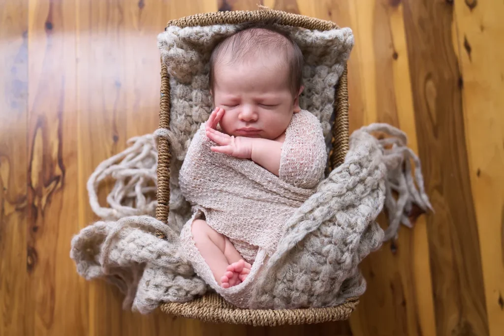 newborn in pink wrap in wooden bowl on floor