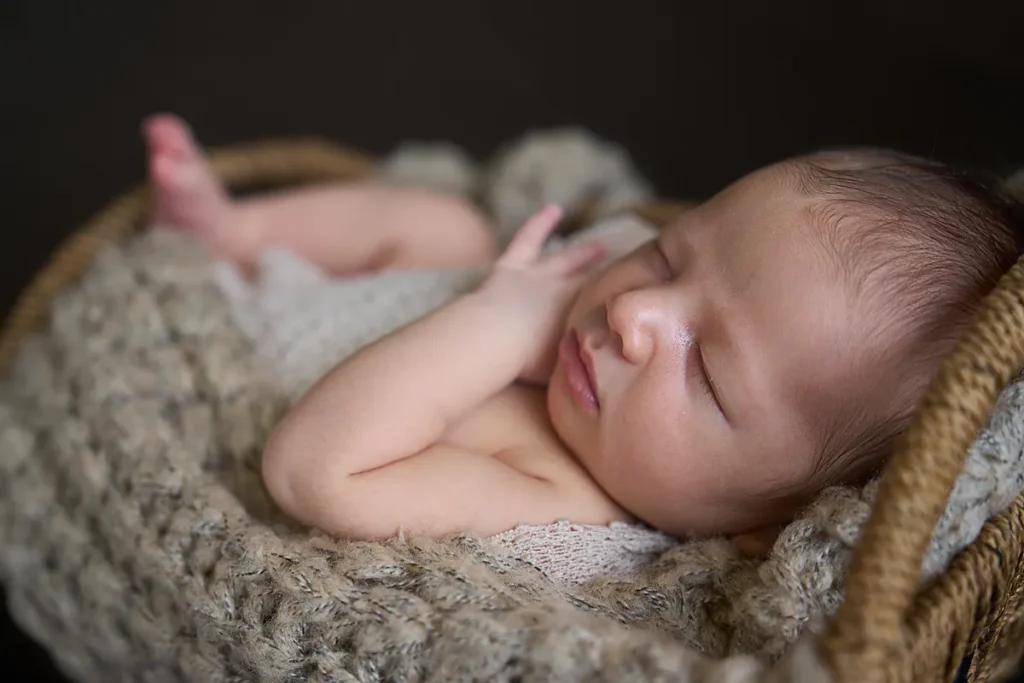 sleeping newborn in grey knit wrap in basket