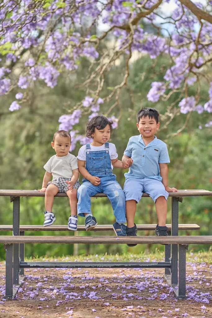 Three boys sitting under purple blossoms