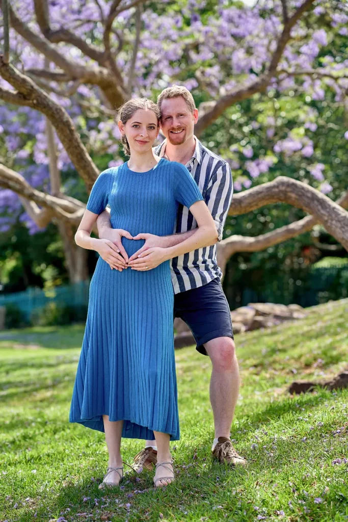 Pregnant woman making heart shape under jacaranda in Hornsby